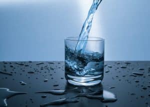 A glass cup sets on a counter as water is poured into it from above.